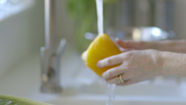Woman washes salad and places in steel colander