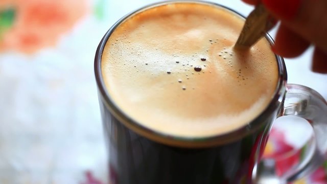 Hand putting sugar cube into a cup of coffee and stirring it. HD