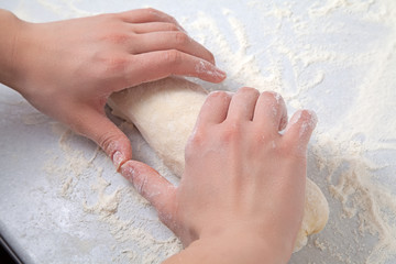 Woman's hands knead dough on a table with flour