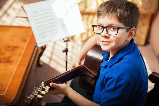Cute kid with glasses learning how to play the guitar at home