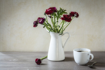 Vase mit Ranunkeln und Tasse Kaffee