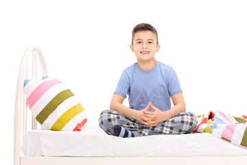 Cute little boy in pajamas sitting on a bed