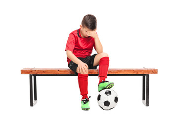 Sad kid in soccer uniform sitting on a bench