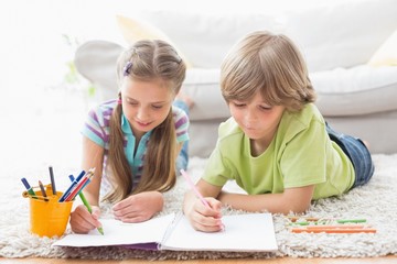 Siblings drawing with colored pencils while lying on rug