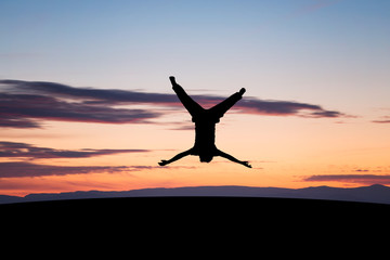 silhouetted young man jumping upside down in sunset