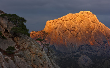 Mountain in orange light. Cliff top Sokol in sunset light against the background of thunderclouds. Crimea, Novy Svet.