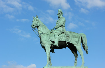 Fototapeta premium The monument of Emperor Wilhelm I. Figure of the Emperor Wilhelm I on a horse on a background of blue sky. Monument is located near the City hall Hamburg-Altona.
