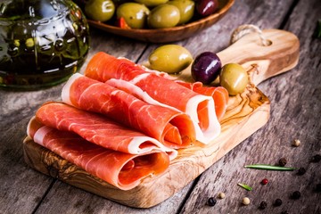 thin slices of prosciutto with mixed olives on a cutting board