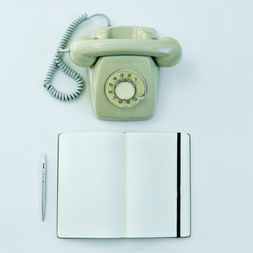 rotary telephone, pen and blank notepad on a table