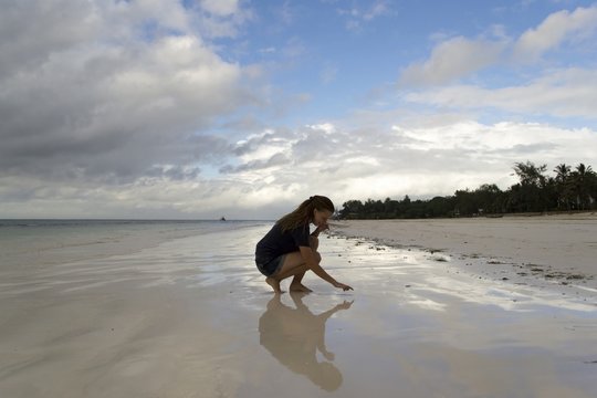 Young woman sitting on beach with reflective sand