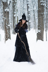 Fototapeta premium Woman in witch's hat holding broom in winter forest