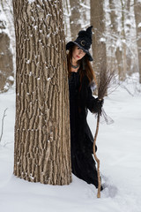 Woman in witch's hat holding broom in winter forest