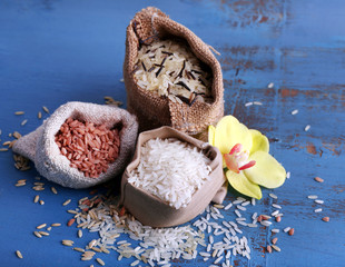 Different types of rice in sacks on wooden background