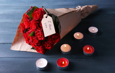 Bouquet of red roses with tag wrapped in paper and candles