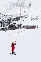 Little girl snowboarding going up a hill on ski tow in French Alps