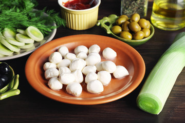 Mozzarella cheese with olives and greens on wooden background