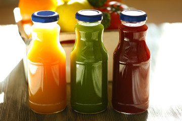 Bottles of juice with fruits and vegetables on table close up