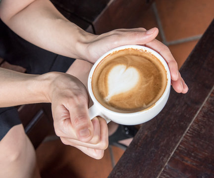 hand holding coffee cup above wooden table,top view
