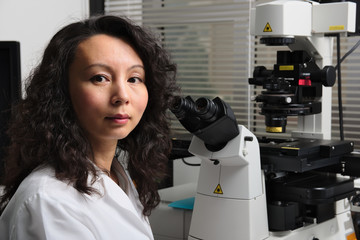 Asian female scientist sitting at microscope