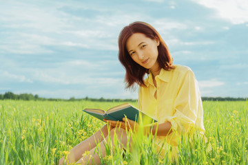 Naklejka na ściany i meble Woman sitting on summer meadow with a book