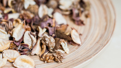 Fragrant blend of natural dried potpourri of berries and fruits in stylish round brown striped wooden plate on tawny brown homogeneous background