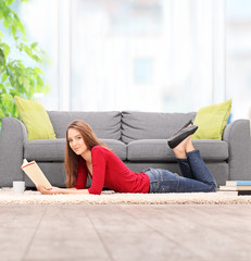 Obraz premium Young woman reading book and lying on the floor