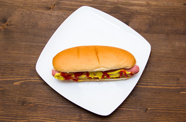 Hot dog on plate on wooden table seen from above