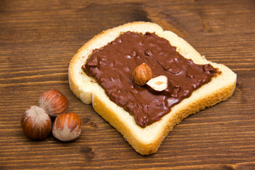 Slice of bread with chocolate with hazelnuts on wooden table
