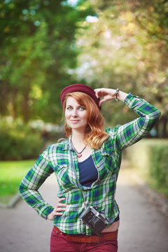 Cheerful hipster redhead girl in hat with retro camera