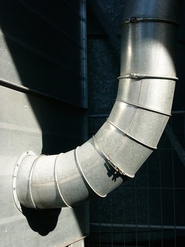 Kr&uuml;mmung eines silber gl&auml;nzenden Abluftrohrs im Sonnenschein in einer Fabrik im Stadtteil Schildfesche in Bielefeld im Teutoburger Wald in Ostwestfalen-Lippe