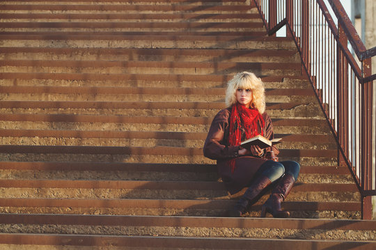 Young girl in leather coat with book seat on stairs bridge in su