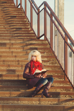 Young girl in leather coat with book seat on stairs bridge in su