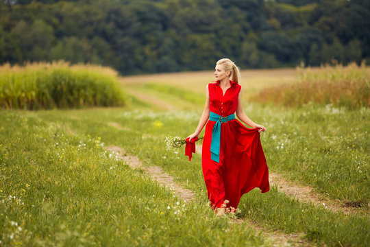 Beautiful young blonde woman in red dress in green field