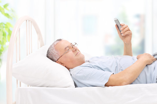 Senior watching something on his cell phone in bed