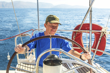 Man skipper at the helm controls sailing yacht.