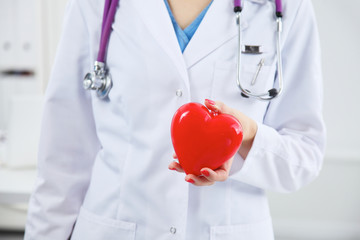 Female doctor with stethoscope holding heart over white