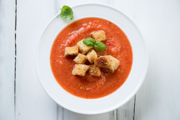 Above view of a glass plate with Gazpacho, white wooden surface