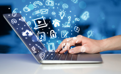 Hand writing on notebook computer with media icons and symbols