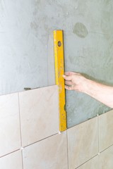 Hand with spirit level against gray wall with tiles