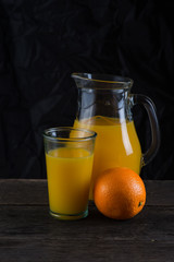 Vintage jug and glass with orange juice, on dark background
