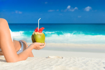 Young woman in swimsuit with coconut cocktail on the beach