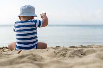 Baby boy with hat sitting on the beach.