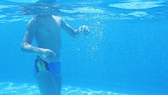 Cute teen boy dives in blue pool jumping in the water