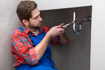 Young plumber is repairing a sink at the bathroom