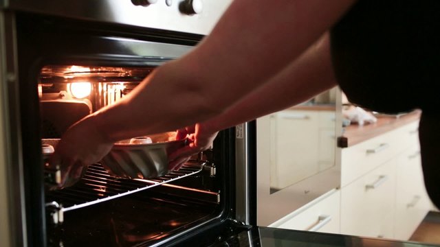 Female baker putting a marble cake into the heaten oven