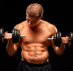 Fototapeta na wymiar Powerful sportsman pumping up biceps muscles with dumbbells