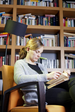 Mujer rubia leyendo libro a la luz de una l&aacute;mpara