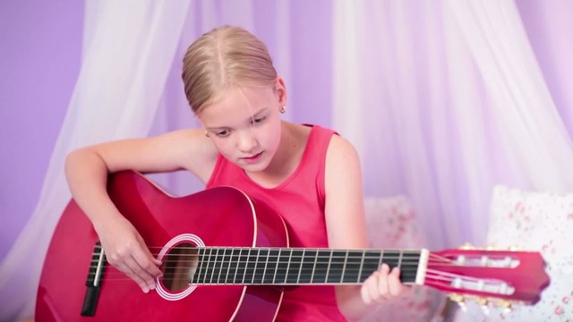 Cute little girl is playing a guitar, practicing at home