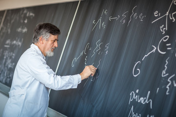 Senior chemistry professor writing on the board while having a c