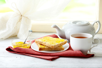 Toasts with honey on plate and cup of tea on light background